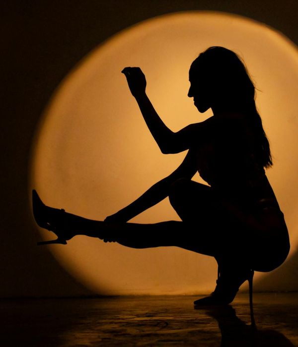 Woman performing a graceful yoga pose in a dark studio with yellow light.